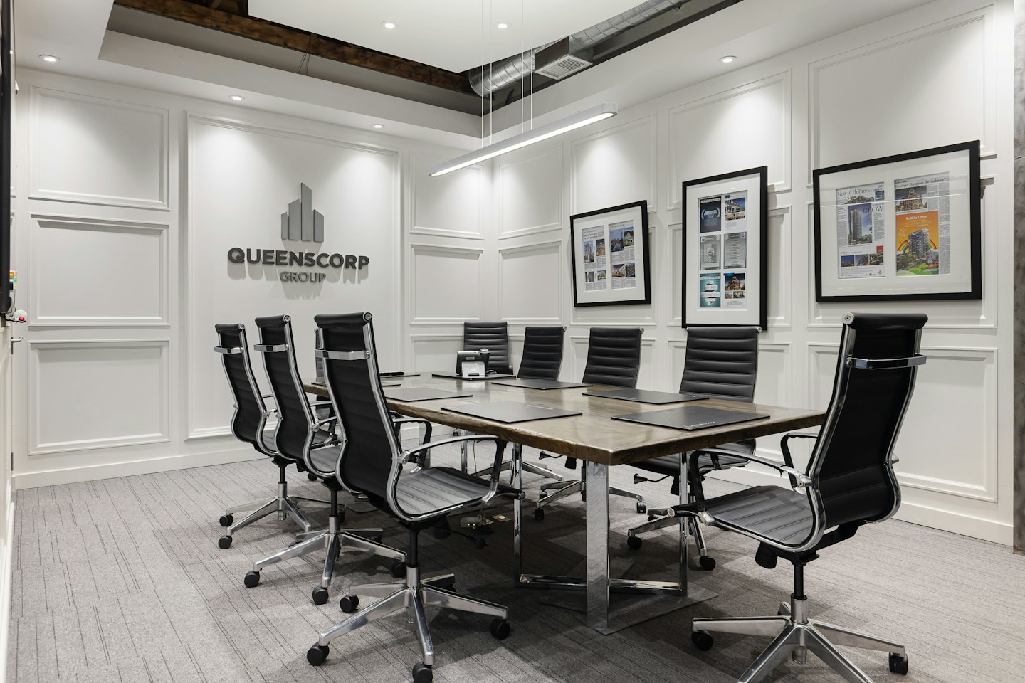 Konferenzraum mit langem Tisch und Queenscorp Group Logo.