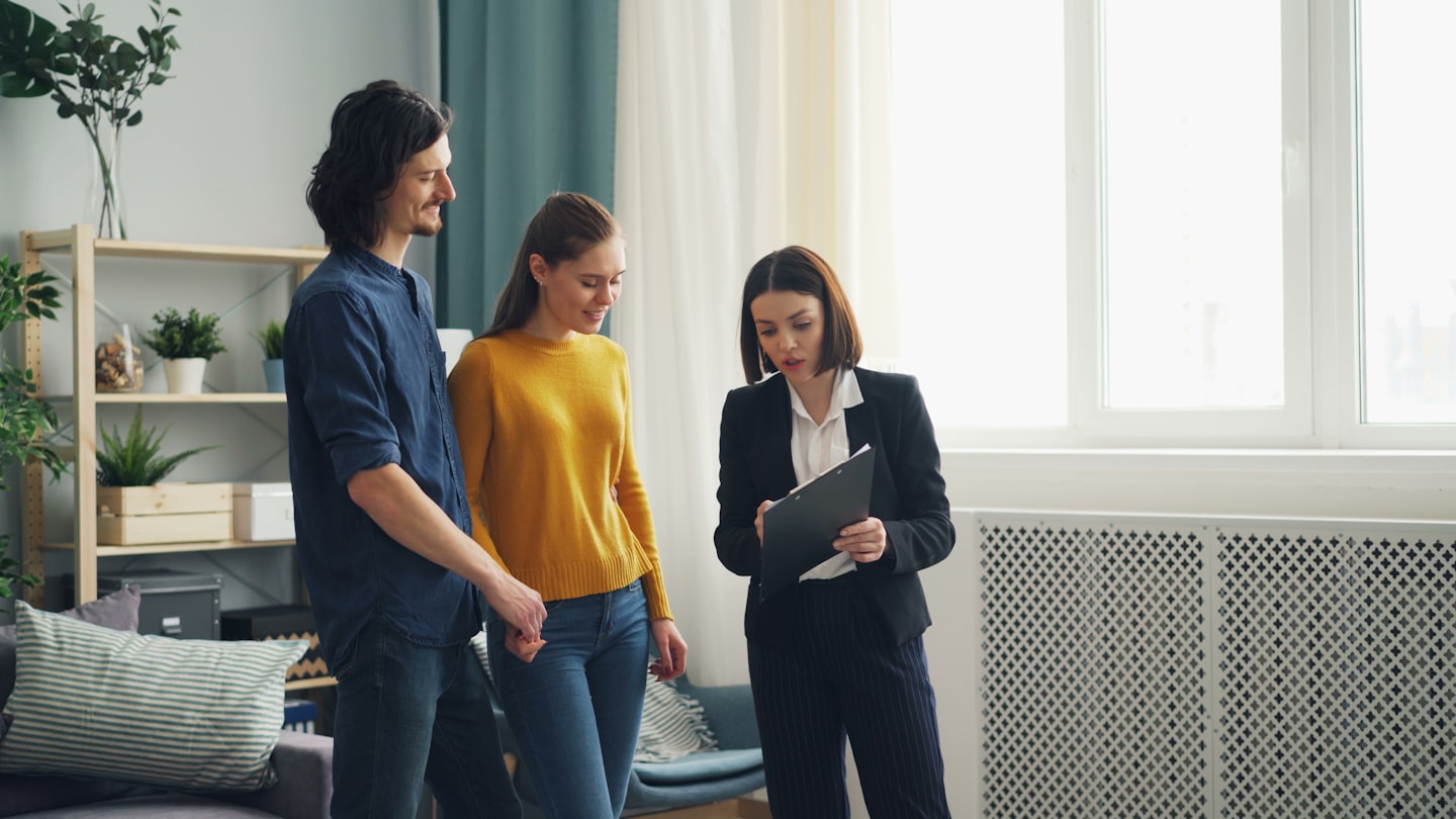 Immobilienmakler zeigt einem Paar in einer modernen Wohnung Dokumente.