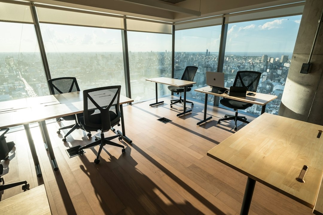 Sunlit modern office with desks by large windows overlooking city.